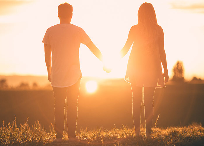 man and woman holding hands facing sunset